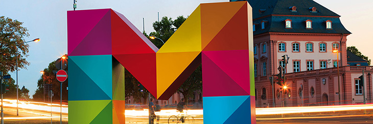 Buntes M-Logo der Unternehmensgruppe Mainzer Stadtwerke vor dem Landtag bei Abenddämmerung